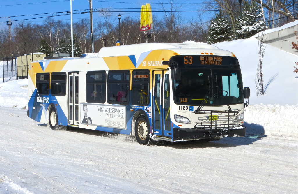 A clean, modern looking bus with yellow and blue X-shaped markings on white, drives through the snow in the centre of the image.