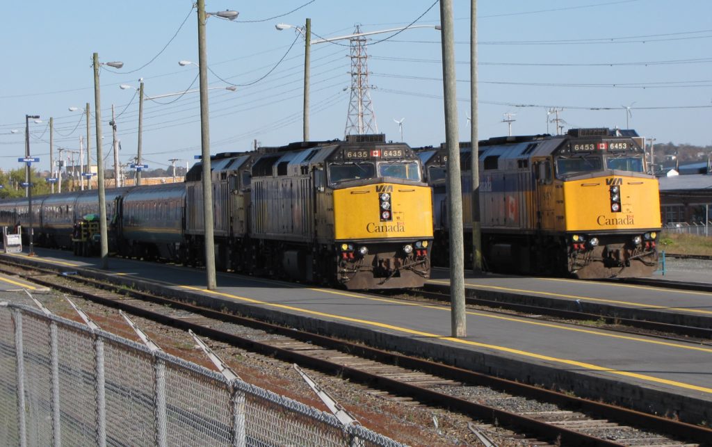 Two yellow VIA Rail trains sit on tracks next to each other at the Halifax station on a sunny day.