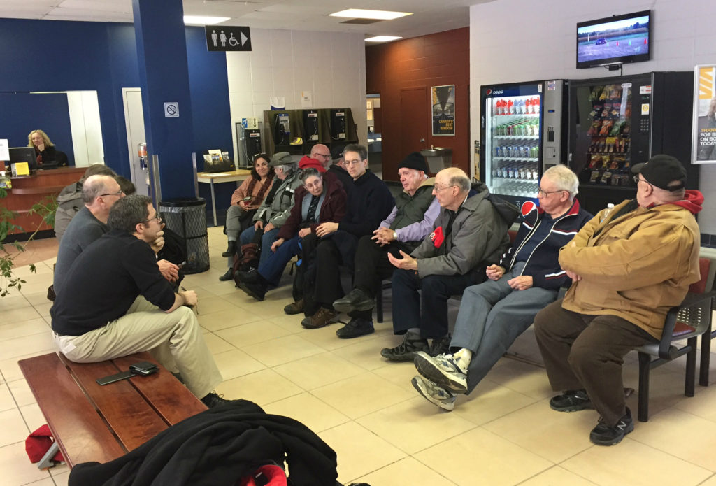 A group of people seated on facing rows of seats in a station waiting room