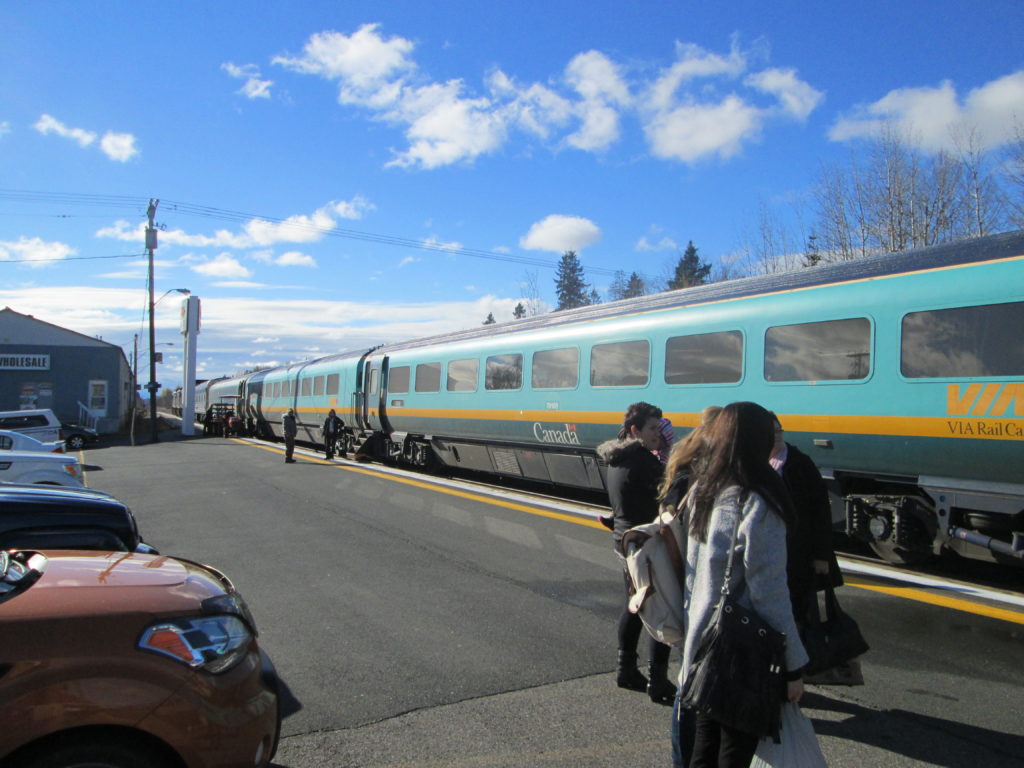 Passengers stand on the platform next to VIA's two-tone teal Renaissance passenger cars
